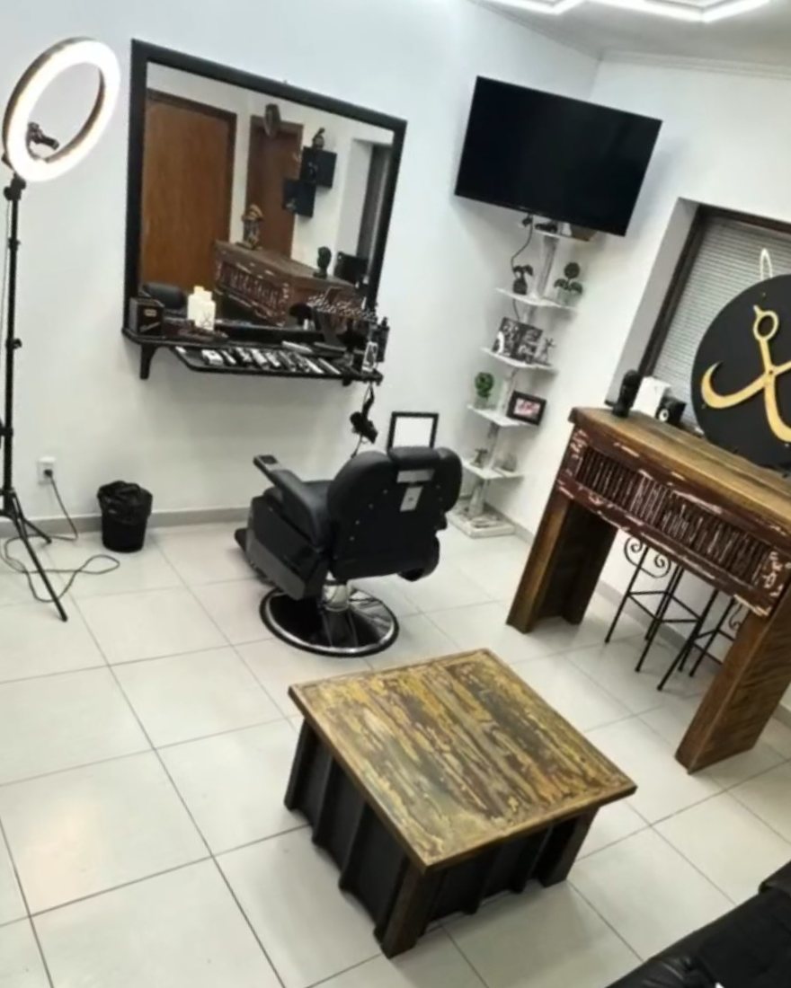 Interior de la barbería: el sillón negro frente al espejo, la tele en la pared y el mostrador de madera con las tijeras del logo.